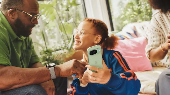 Seorang anak menunjukkan sesuatu di ponsel Pixel kepada orang dewasa yang duduk di sebelahnya.