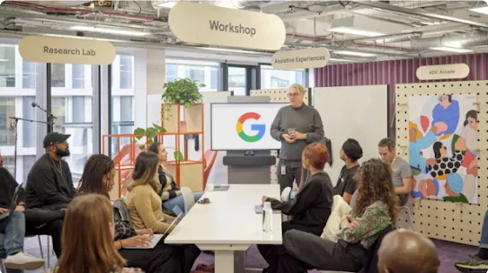 Ten Googlers sit around a table at the Accessibility Discovery Centre, a man stands speaking at the end of it 