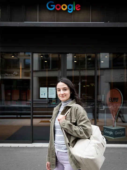 Une ancienne apprentie avec un sac à dos se tient devant le siège de Google en Suisse.