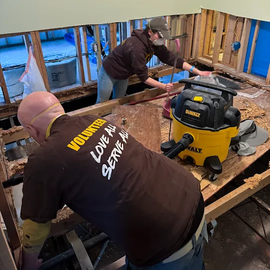 Two people wearing masks doing construction inside of a building with construction equipment on the table.