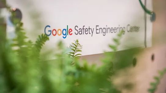 A white sign that reads "Google Safety Engineering Centre". A green plant is partially visible in the foreground.