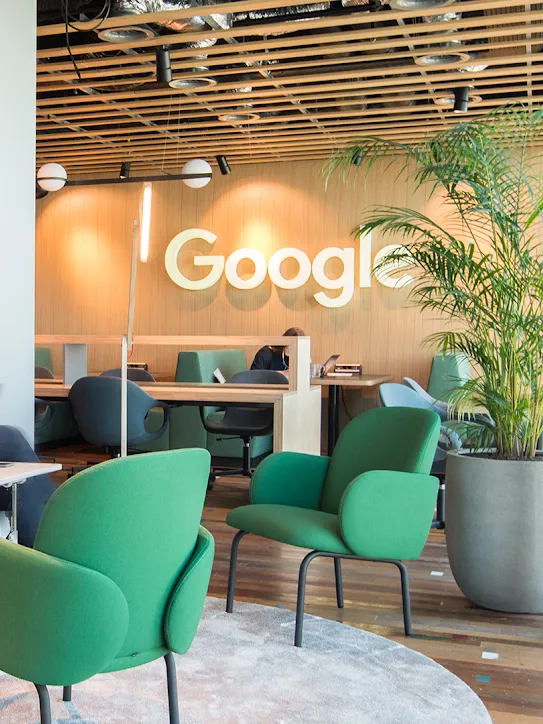 Dua orang duduk di ruang kerja dengan logo Google di latar belakang.