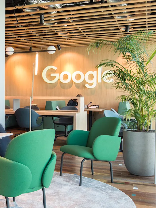 Deux personnes assises dans un espace de travail, avec le logo Google en arrière-plan.