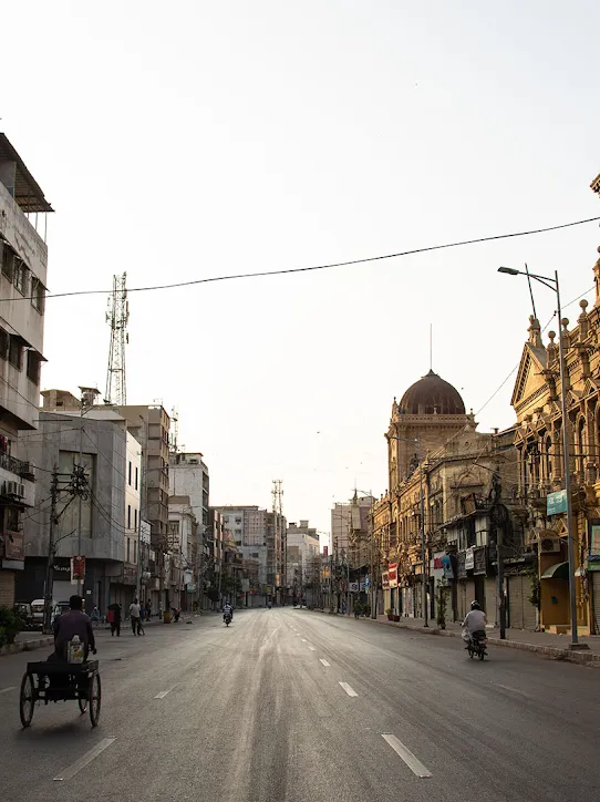 A street with various buildings, and people riding in bikes and other vehicles.