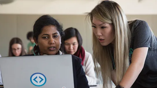 Two people look at a computer screen in a classroom setting.